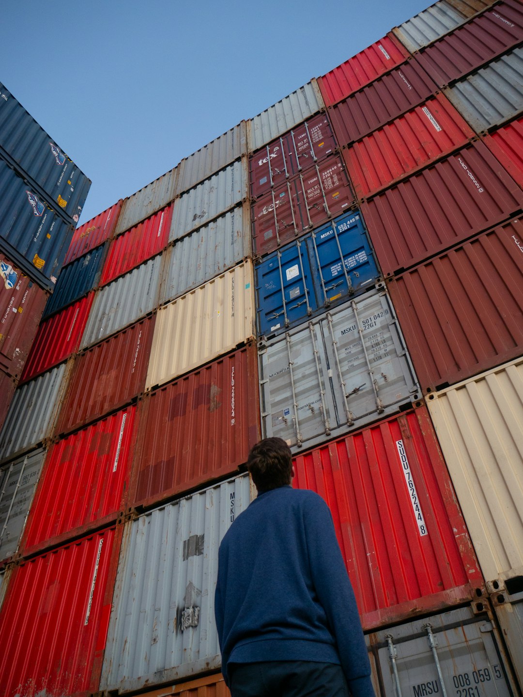 man-in-black-jacket-standing-in-front-of-red-and-blue-intermodal-containers-xsswba4rb6e